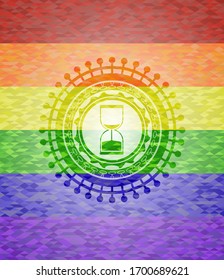 sand clock icon inside emblem on mosaic background with the colors of the LGBT flag