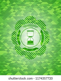 sand clock icon inside green emblem with triangle mosaic background