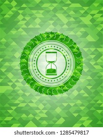 sand clock icon inside green emblem with triangle mosaic background