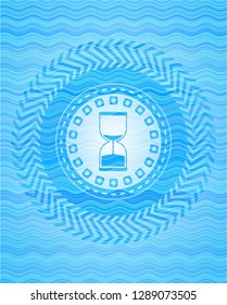 sand clock icon inside sky blue water wave emblem.