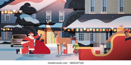 santa claus with deer and elf preparing gifts happy new year merry christmas holidays celebration concept night street with decorated houses full length horizontal vector illustration