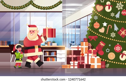 santa claus with elf helper put present under decorated fir tree in modern office merry christmas happy new year holidays concept flat horizontal