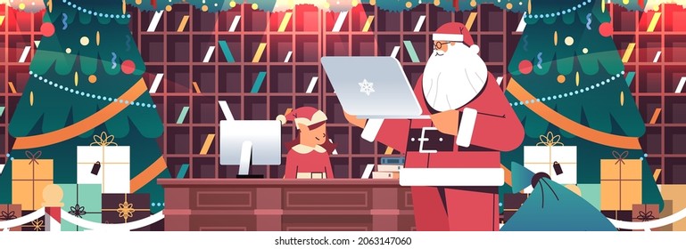 Santa Claus With Elves Using Laptop Preparing Gifts For New Year And Christmas Holidays Celebration Modern Workshop