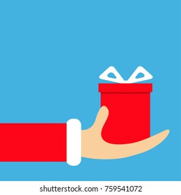 Santa Claus hand holding gift box with bow. Merry Christmas. Red costume fur. Giving giftbox present. Cute cartoon funny character Winter blue background Flat design. Greeting card Vector illustration