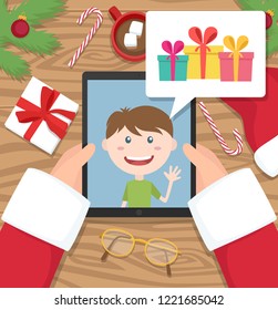 Santa claus is holding tablet on wooden desk and is having conversation with young kid who talks about gifts he would like to get at christmas. Flat design vector illustration. 