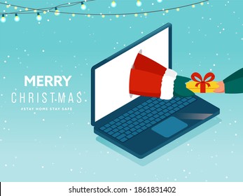 Santa Giving Gift Online To Person Through Laptop And Lighting Garland On Snowfall Blue Background For Merry Christmas, Stay Home and Stay Safe.