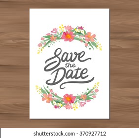 Save the date wedding invitation with watercolor flowers and hand drawn lettering. Card template on a wooden background