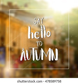 Say hello to autumn. Handwritten autumn greeting card. Modern calligraphy on blurred background.