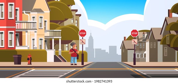 schoolboy with backpack standing near red stop road sign on city street road safety concept full length horizontal