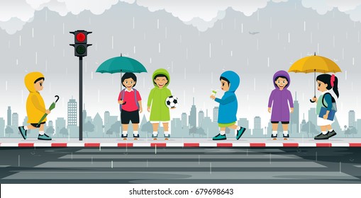 Schoolboy wears a raincoat and holds an umbrella to protect the rain.