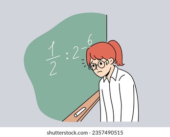 Schoolgirl standing near chalkboard gets, upset because doesnt know solution of mathematical example and needs help of tutor. Girl is having trouble getting elementary school mathematical education