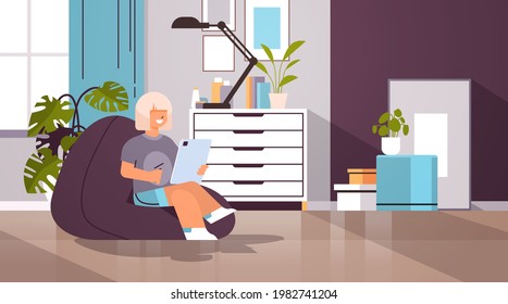 schoolgirl using tablet pc happy girl sitting on beanbag and doing homework education concept living room interior