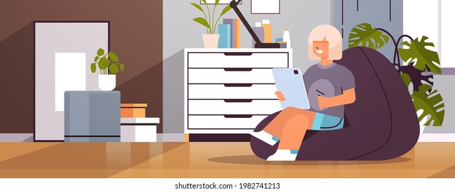 schoolgirl using tablet pc happy girl sitting on beanbag and doing homework education concept living room interior