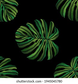 Seamless pattern of embroidered green tropical monstera palm leaves on black background. Embroidery stitches imitation