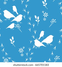 Seamless pattern with silhouetted birds, floral motifs and bird tracks. White silhouettes on a blue background.