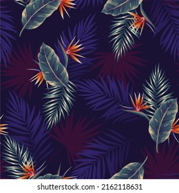 Seamless pattern of tropical dark leaves of palm trees and flowers bird of paradise (strelitzia) on a blue background. Design for paper, cover, fabric, interior decor and other users.