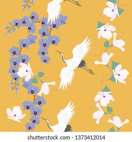 Seamless vector illustration with birds cranes, hibiscus flowers and orchid on a yellow background. For decorating textiles, packaging, web design.