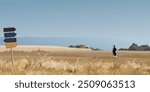 Seashore landscape with a woman walking on grass field in autumn season have direction sign pole at foreground graphic illustration. Coastline have blue sky background.