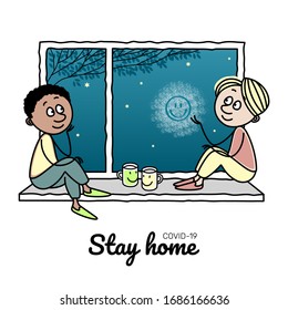 Self-isolation from a pandemic. Two young people are sitting on the windowsill. Smiling face on a window pane. Coronavirus pandemic. Stay quarantined at home to stop the spread of the virus