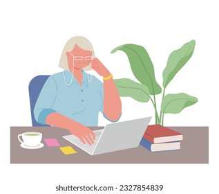 Senior character at work. An elderly woman wearing glasses is working on a computer at a desk piled with books.