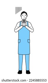 A senior man in an apron apologizing with his hands in front of his body.
