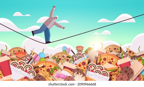 senior man balancing on rope above junk food assortment of fast food unhealthy nutrition junkfood addiction concept