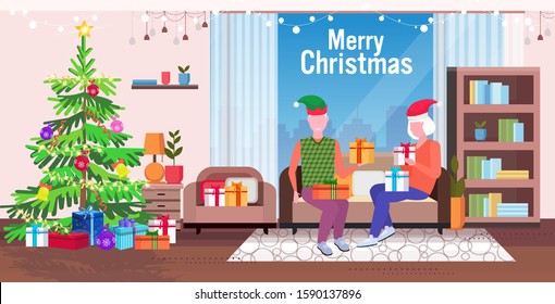 senior man in elf hat giving present gift box to mature woman family sitting on couch celebrating merry christmas happy new year winter holidays concept modern living room interior full length