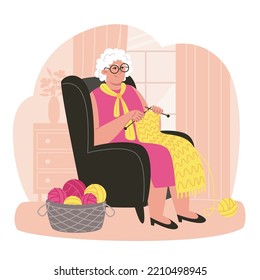 Senior woman sits in an armchair and knits a scarf in a cozy room