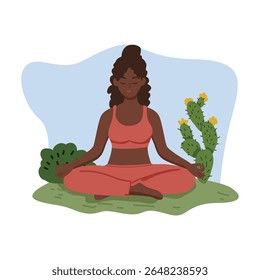 Mulher serena com pele escura meditando em posição de lótus na grama verde vestindo traje atlético de coral com um cacto e arbusto atrás dela, evocando tranquilidade e equilíbrio para conteúdo de bem-estar.