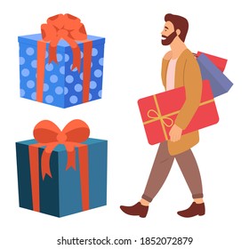 Serious bearded man with presents in his hands. Young handsome fashion shopper guy is standing near big gift boxes. Male character in store is buying presents for the holliday and holding purchases