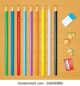 A set of colored pencils with eraser, sharpener and pencil parings on a wooden desktop.