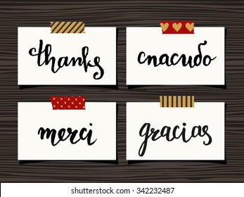 A set of four Thank You notes on wood background. Hand lettered "Thank you" in different languages - "Spasibo"(Russian), "Merci"(French), "Gracias"(Spanish).