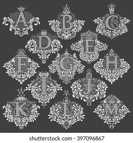 Set of heraldic monograms in coats of arms form. White floral decorative stamps of letters from A to M. Isolated tattoo labels in vintage baroque style.