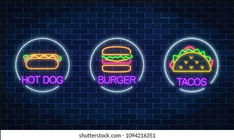 Set of three neon glowing signs of burger, hot dog and tacos in circle frames on a dark brick wall background. Fastfood light billboard symbol. Cafe menu item. Vector illustration.