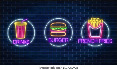Set of three neon glowing signs of french fries, burger and soda drink in circle frames on a dark brick wall background. Fastfood light billboard symbol. Cafe menu item. Vector illustration.