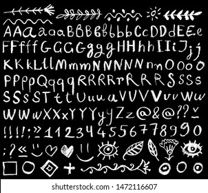 Set of white letters and symbols written with chalk on a chalkboard. Numbers, signs, and decorative elements: flowers, leaves, sun, eye, waves, dots.