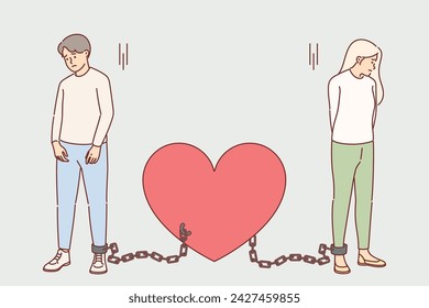 Shackled couple in love suffers from lack personal freedom, stands tied with chains to heart. Sad bride and groom need help from psychologist because oppressive relationship that is destroying couple