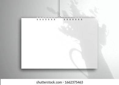 The shadow of the bouquet in a ceramic jug falls on a white blank spiral calendar. Realistic mockup for design