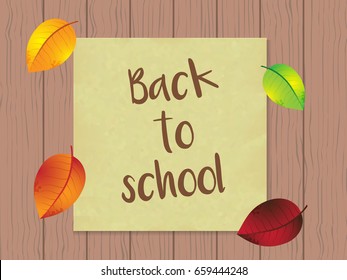 Sheet for notes on the wooden wall with the text `back to school` and leaves in vintage style