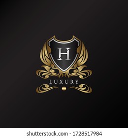Shield logo in gold color with letter H Logo. Elegance logo vector template made of wide silver alphabet font on shield frame ornate style.
