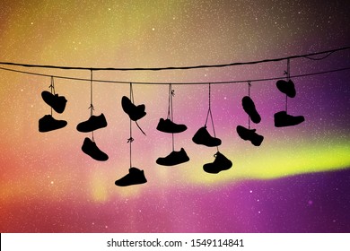 Shoes on wires at night. Vector illustration with silhouette of old shoes hanging on power lines. Northern lights in starry sky. Colorful aurora borealis