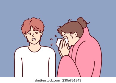 Sick woman sneezes standing near guy afraid of contracting dangerous flu or cold. Sick girl with handkerchief is wrapped in blanket and needs treatment and antibiotics to fight infection.