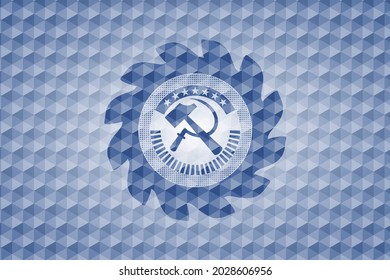ícono de hoz y martillo dentro del emblema azul o placa con fondo de patrón geométrico. 