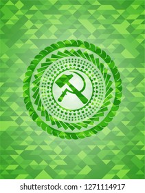 sickle and hammer icon inside green emblem with triangle mosaic background