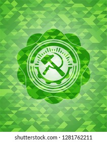 sickle and hammer icon inside green emblem with triangle mosaic background