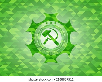 ícono de hoz y martillo dentro del emblema verde con fondo de mosaico triangular. 