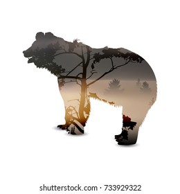 Silhouette of bear with panorama of mountains and pine forest. A large tree in the foreground. Lights of sunset. Thick fog.