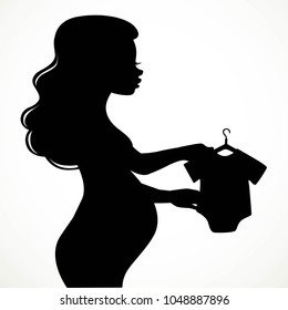 Silhouette of a beautiful young pregnant womanconsiders infant body on a hanger isolated on white background
