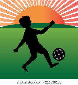 A silhouette of a boy playing with a ball in a play field. An outdoor playground and a proper sunset time in the back . The sun is orange with long sun rays.