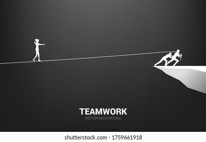 Silhouette of businesswoman walking on rope walk way pulled by team.Concept for teamwork and team support..